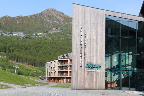 A hotel with a wooden facade and a glass entrance, surrounded by a mountainous landscape.