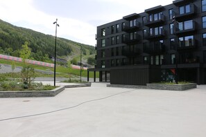 A modern building with multiple balconies, a paved area, and a train track in the background. - Stylish Apartment in Hemsedal Ski Resort – Ski In/Ski Out (Hemsedal)