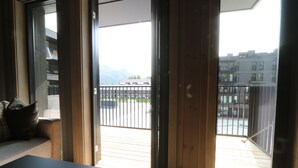Una habitación con puerta corrediza de vidrio que da a un balcón con vistas a edificios y montañas.
