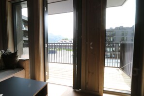 Una habitación con puerta corrediza de vidrio que da a un balcón con vistas a edificios y montañas.