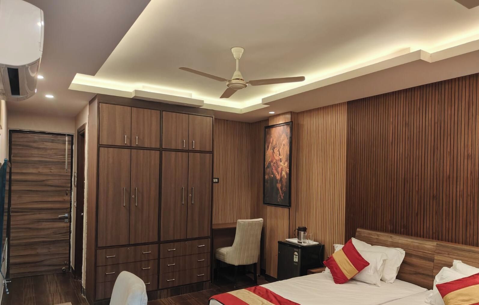A hotel room with a bed, wardrobe, ceiling fan, and artwork on the wall.