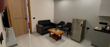 A compact living space with a sofa, two chairs, a coffee table, a refrigerator, and a wooden door.