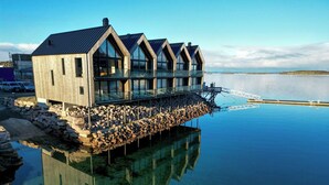 Ein Holzhaus mit großen Fenstern und einem Balkon, das auf Stelzen über Wasser gebaut ist.
