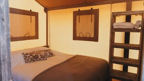 Uma cama de solteiro com travesseiro estampado, uma escada de madeira e duas molduras com imagens na parede.