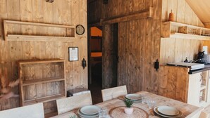 Un coin repas rustique, avec une grande table en bois dressée pour quatre personnes, entourée de chaises, et un mur en bois agrémenté d’étagères.