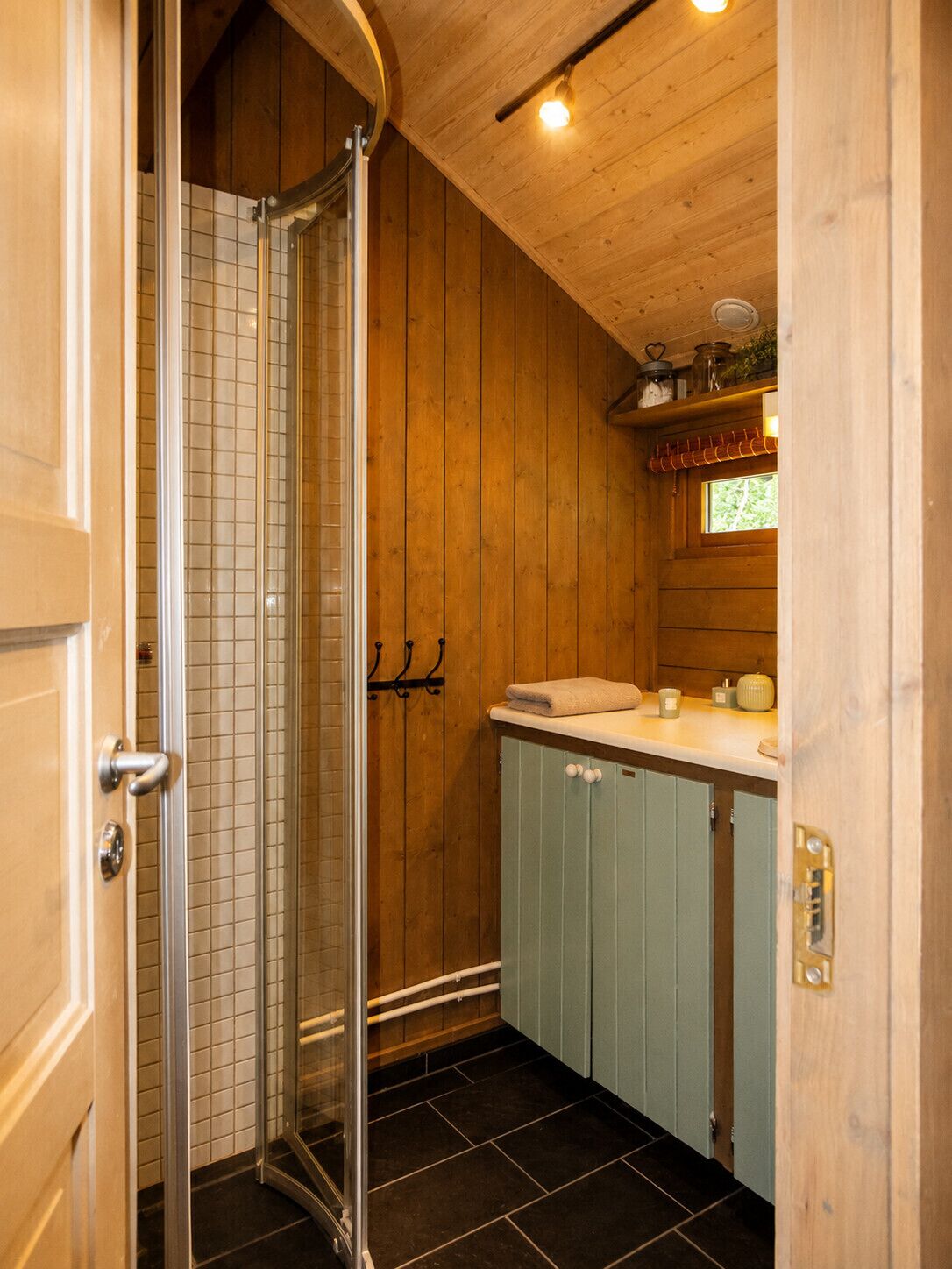 Interior de madera con cabina de ducha de vidrio, lavamanos y armarios.