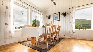 A dining area with a table set for four, wooden chairs, a black rug, and a view of greenery outside. - Private cabin by the sea, Lofoten (Vestvågøy)