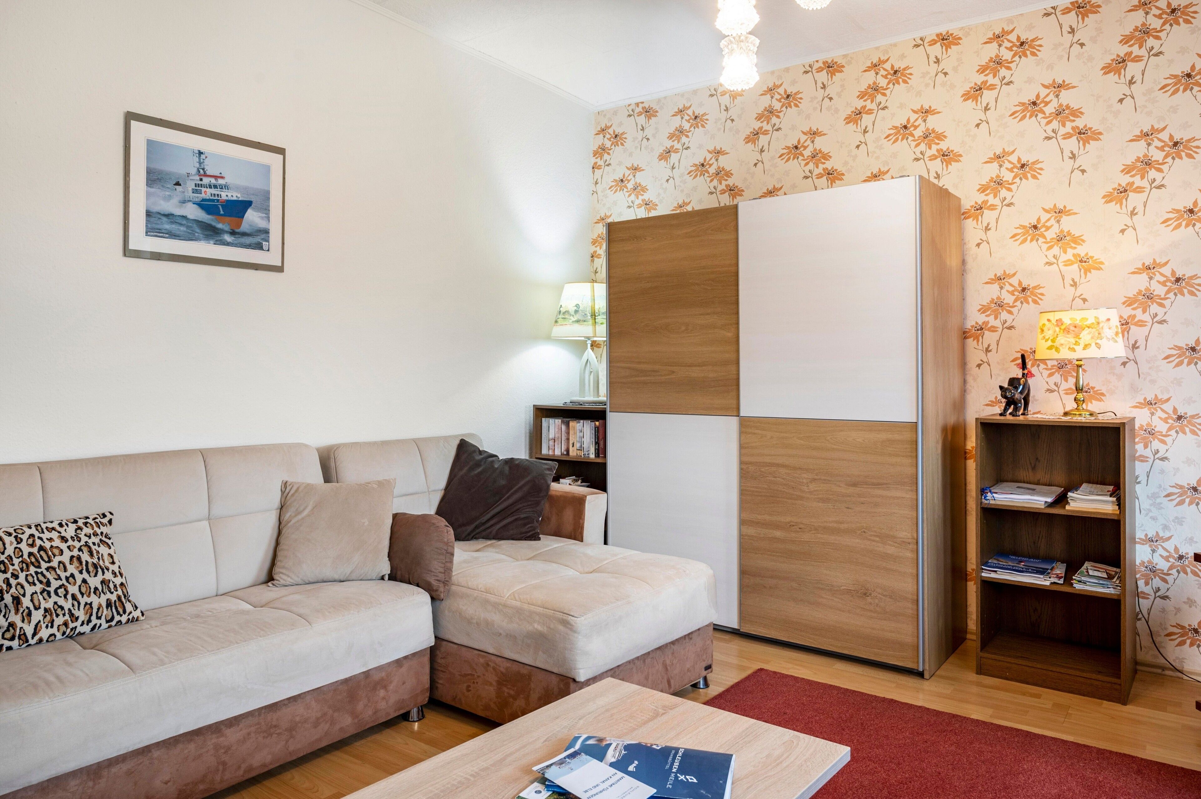 Ein Wohnzimmer mit einer Couch, einem Couchtisch, einem Bücherregal und einer Wand mit Blumenmuster-Tapete.