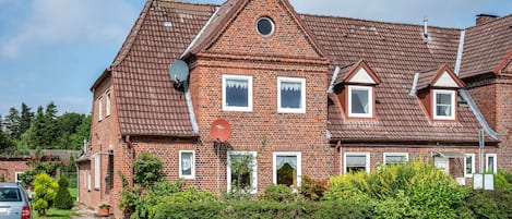 A two-story brick house with a sloped roof, satellite dish, and a small garden area.