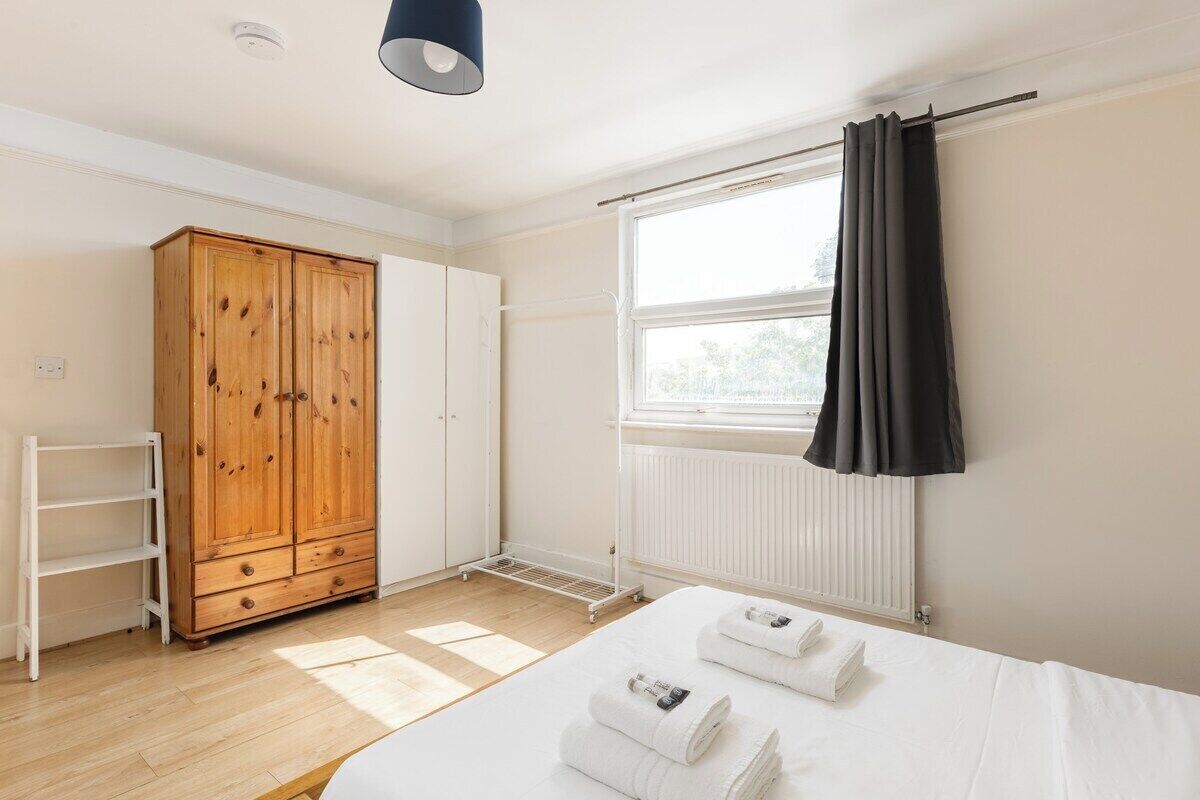 Une chambre à coucher avec un lit, une armoire, un radiateur et une fenêtre avec des rideaux.