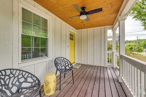 Eine überdachte Veranda mit Deckenventilator, zwei Stühlen, einem gelben Laternen und einer gelben Tür.