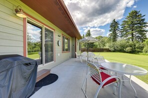 Eine überdachte Terrasse mit Tisch, Stühlen, einem Grill und Blick auf die umliegende Grünfläche.
