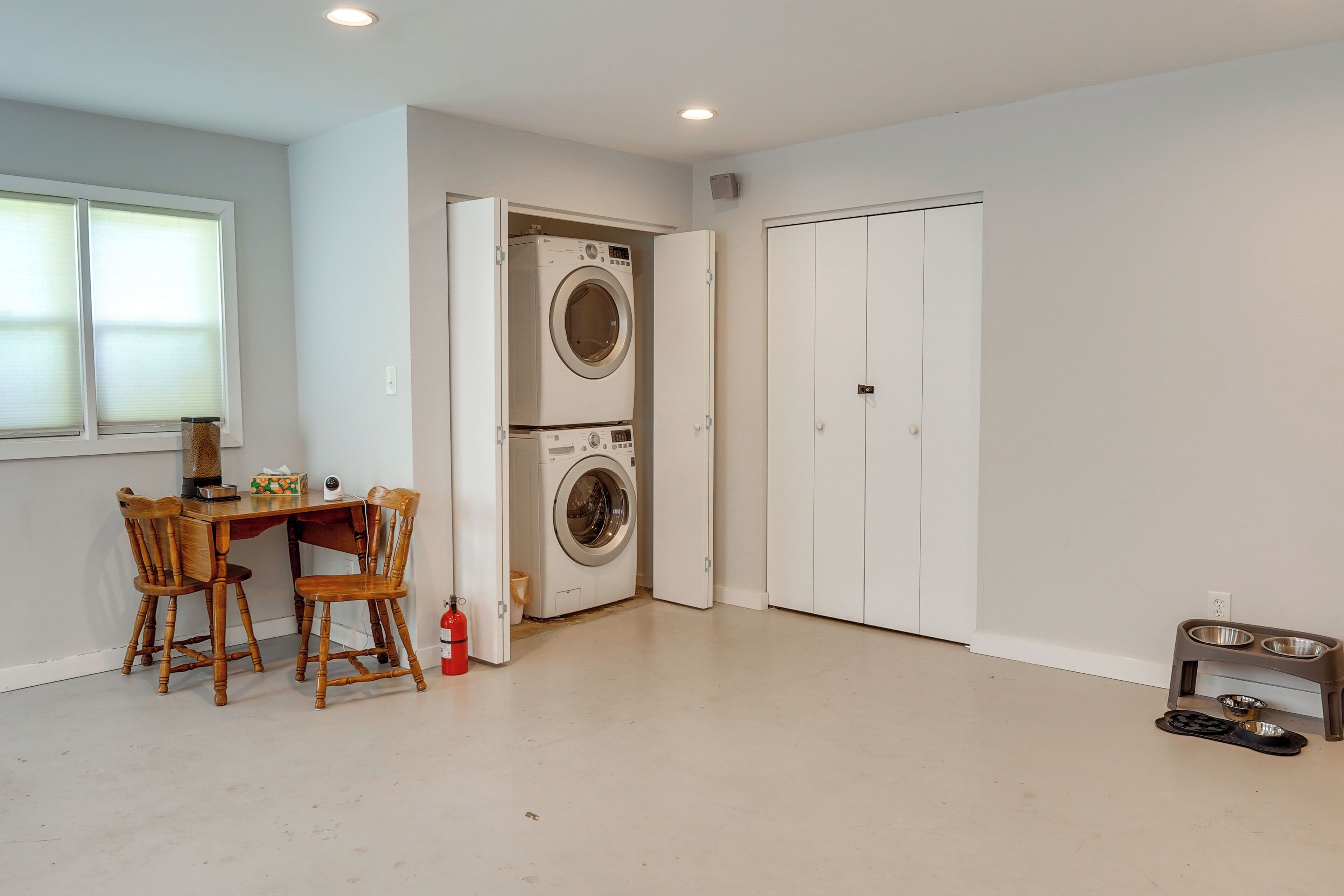A laundry room with two stacked washing machines, a table with chairs, a fire extinguisher, and a pet feeding station.