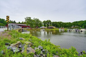 A riverside view with a wooden bridge, boats, and buildings in the background.