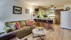Un salon comprenant un canapé, une table basse et un coin cuisine avec un réfrigérateur, une cuisinière et des chaises.