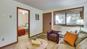 Un salon comprenant un canapé, un fauteuil, une table basse avec un panier, une lampe et une fenêtre donnant sur un beau paysage.