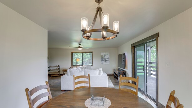 Un coin repas avec une table en bois, des chaises, un lustre et une vue sur un salon comprenant un canapé blanc et un téléviseur.