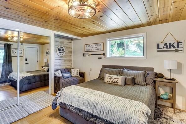 Quarto com uma cama grande, mesa de cabeceira, espelho e janela com vista para árvores.