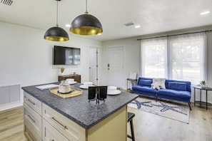 A modern kitchen with granite countertops, a central island, pendant lighting, and a dining area with a blue sofa and a small side table. - Steinhatchee River Hideaway, 1 Mi to the Water! (Steinhatchee)