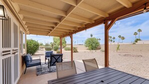 En overdækket terrasse med et bord og stole, udsigt til palmer og et ørkenlandskab.