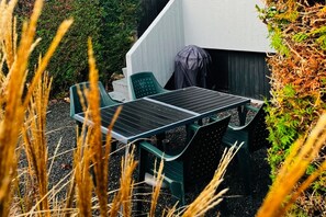 Un espace extérieur aménagé avec une table et des chaises, entouré de plantes et bordé d’un mur blanc.