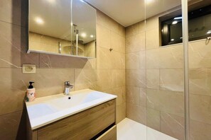 Une salle de bain avec un lavabo blanc, un meuble-lavabo en bois, un miroir et des murs recouverts de carreaux beiges.
