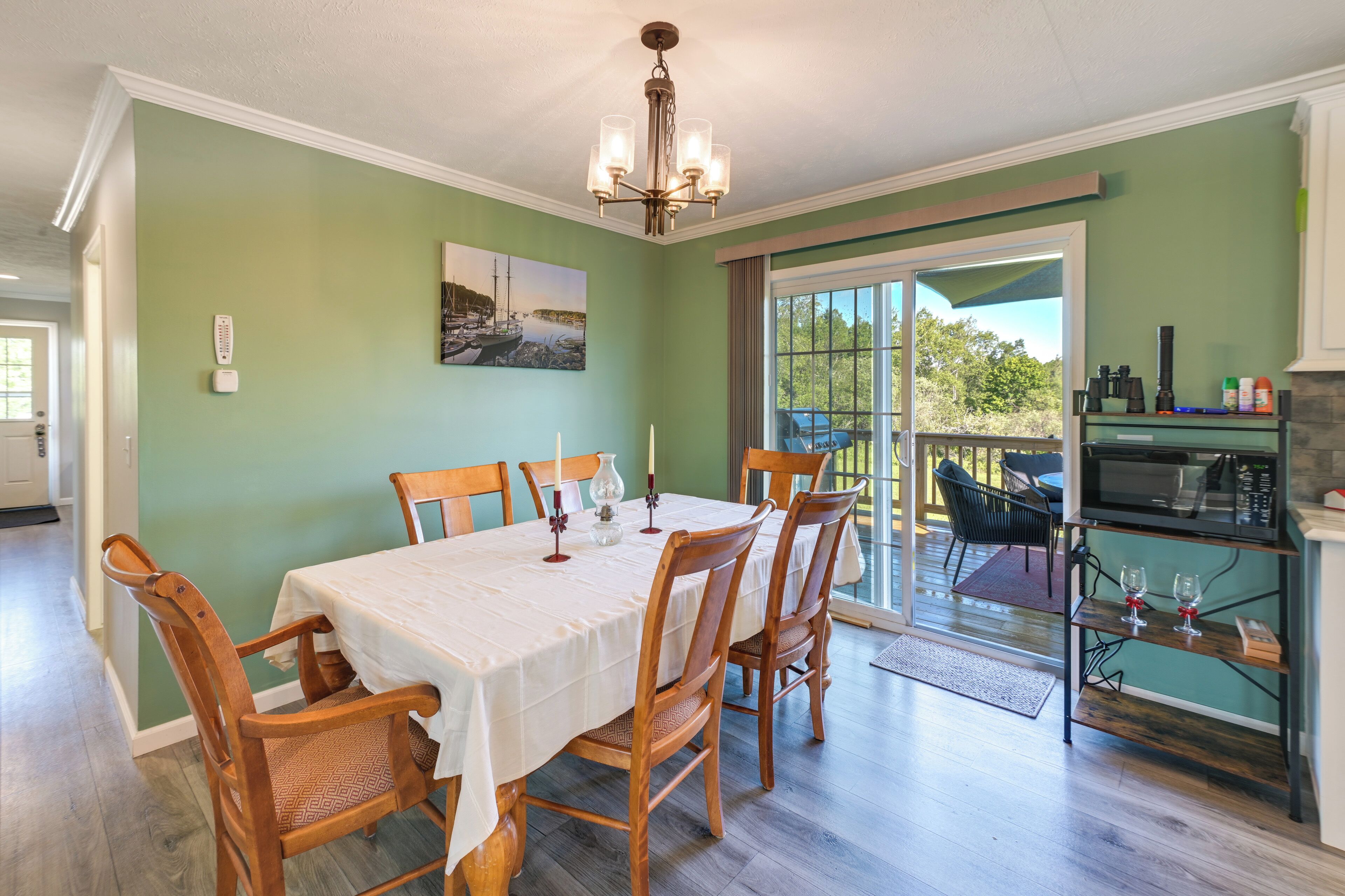 Un coin repas avec une table dressée pour six personnes, des chaises en bois, un lustre et, par une porte vitrée, une vue sur un patio extérieur.