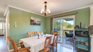 Comedor con una mesa dispuesta para seis personas, sillas de madera, una araña y vistas a un patio exterior a través de un ventanal.