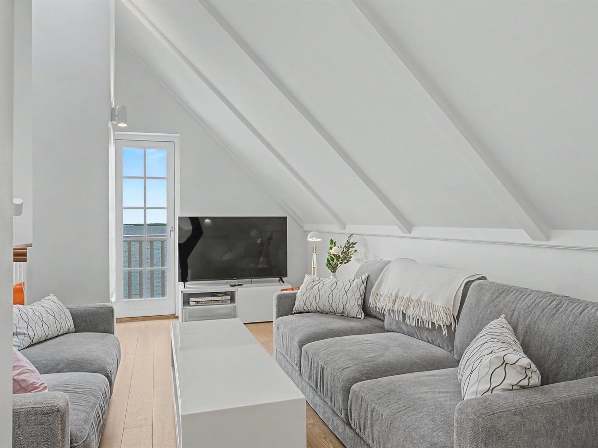 A modern loft bedroom with a large window, a flat-screen TV, and a cozy seating area.