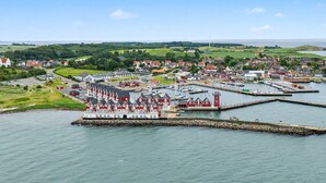 En kystby med et markant bygningskompleks med røde tage ved vandet, en lysthavn og et fyrtårn i det fjerne.