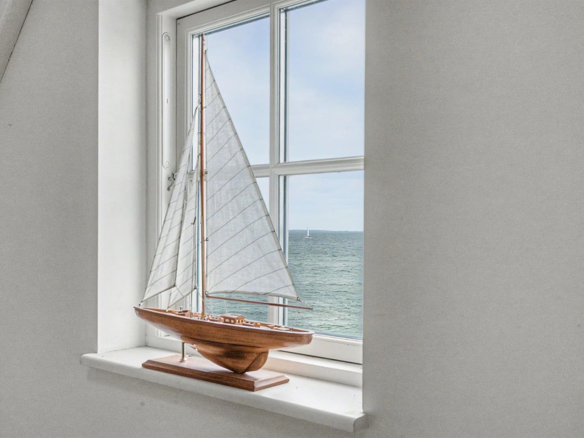 Ein Modellsegelboot auf einem Holzständer neben einem Fenster mit Blick auf das Meer.