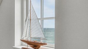 En modelsejlbåd på et træstel ved et vindue med udsigt til havet.
