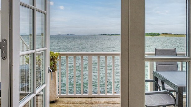 En balkon med udsigt over vandet, et bord og stole.