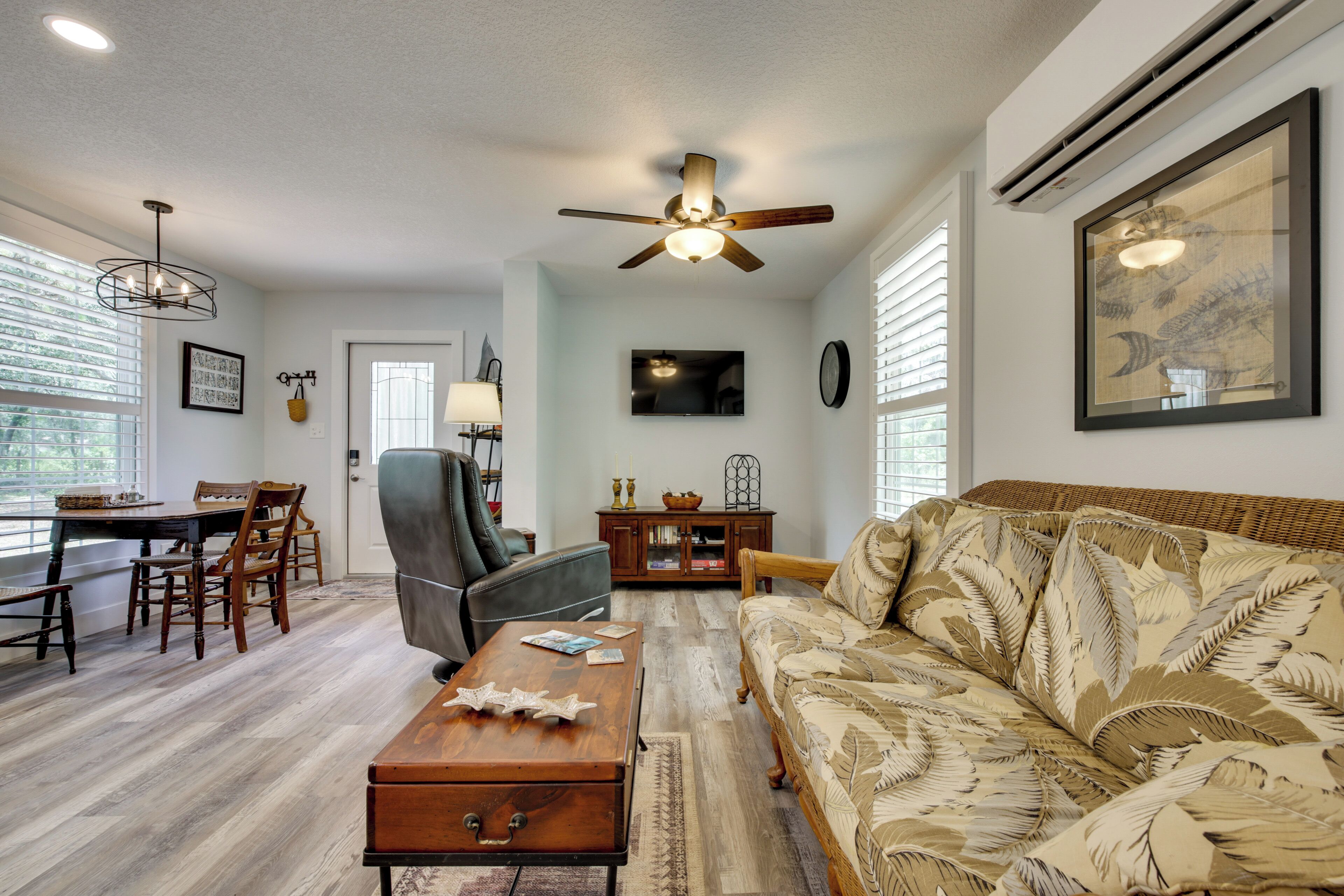 A living room with a sofa, a coffee table, a dining table with chairs, a ceiling fan, and a wall-mounted TV.