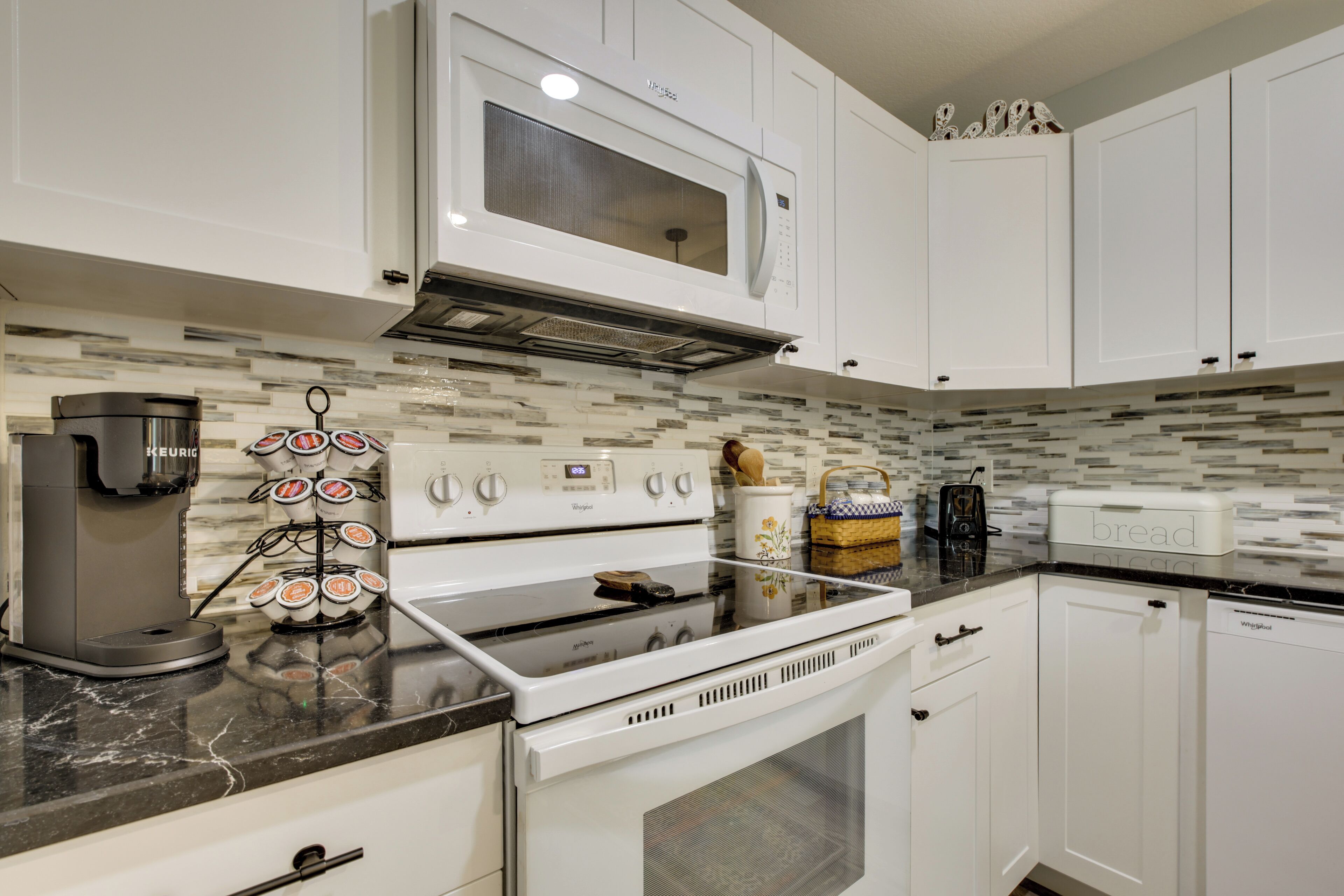A modern kitchen with white cabinets, a built-in microwave, a coffee maker, and a bread box.