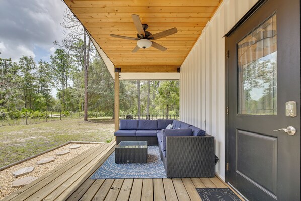A covered porch with a ceiling fan, a dark-colored door, and a blue outdoor seating area. - 6 Mi to Three Sisters Springs! Extended Getaway (Homosassa)