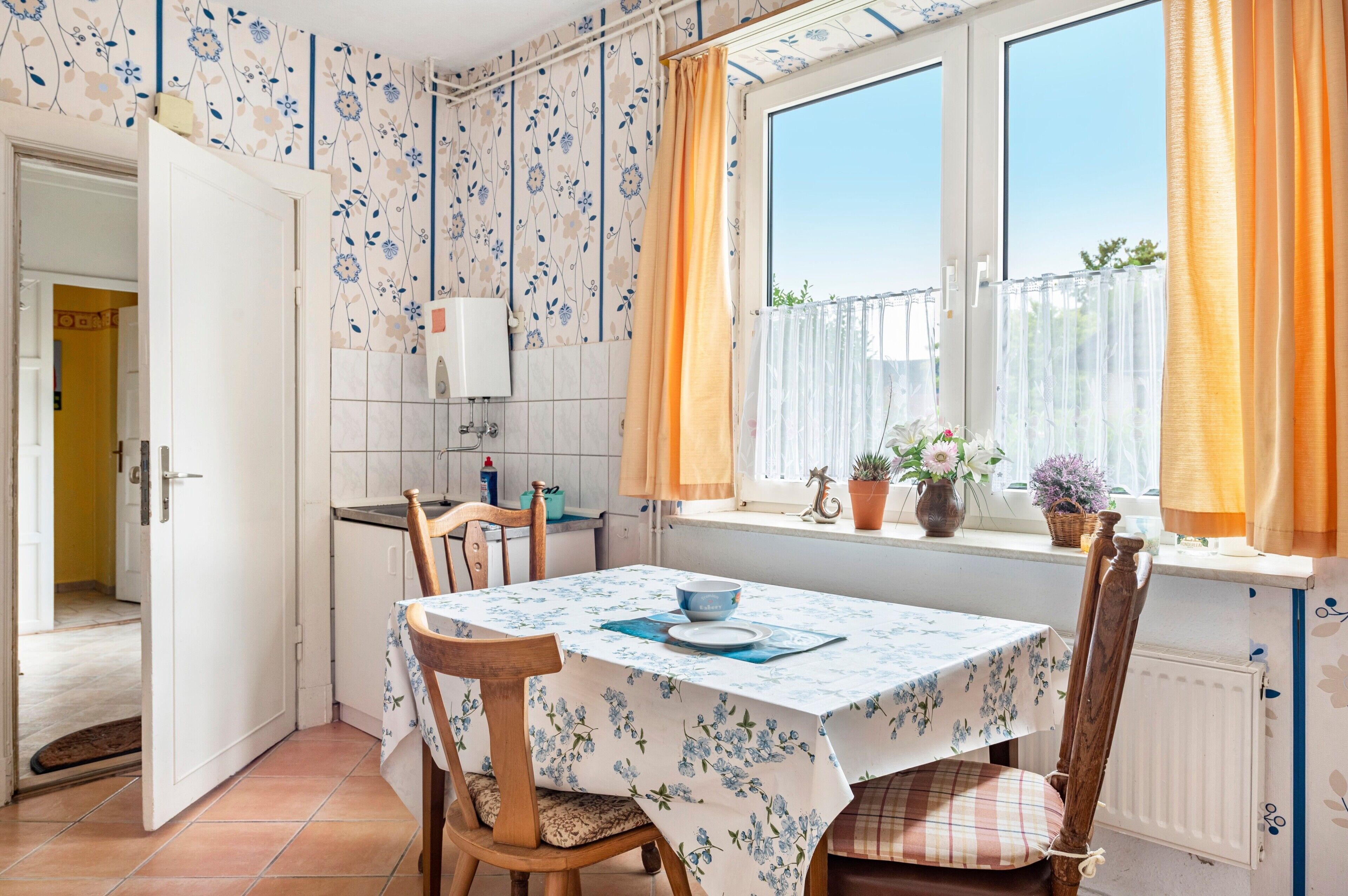 Eine Küche mit Esstisch, Stühlen, einem Fenster mit Vorhängen und Blick ins Grüne.