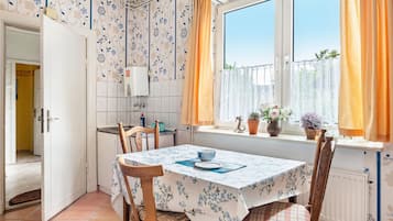 A kitchen with a dining table, chairs, a window with curtains, and a view of greenery outside.