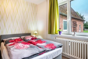 A bedroom with a bed, a window with curtains, and a radiator. - Holiday Apartment for 3 Guests (45 m²) in Brunsbüttel (Brunsbüttel)