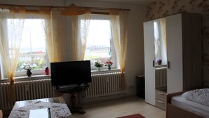 Una habitación con cama, televisión, radiador y ventana con cortinas.