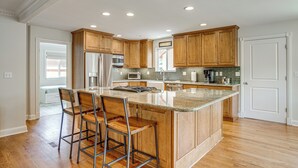 Una cocina moderna con armarios de madera, una isla central con taburetes de bar, electrodomésticos de acero inoxidable e iluminación empotrada en el techo.