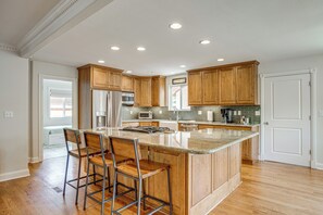A modern kitchen with wooden cabinets, a central island with bar stools, stainless steel appliances, and recessed ceiling lighting. - Family-Friendly Denver Home w/ Patio + Yard (Denver)