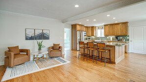 Una cocina amplia con gabinetes de madera, una isla central con taburetes, un comedor con mesa y sillas, y un gran ventanal que proporciona luz natural.