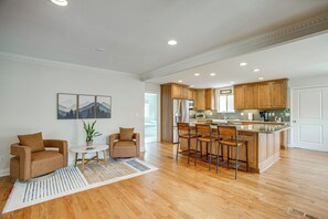 A spacious kitchen with wooden cabinets, a central island with bar stools, a dining area with a table and chairs, and a large window providing natural light. - Family-Friendly Denver Home w/ Patio + Yard (Denver)