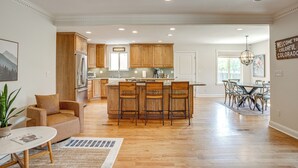 Una cocina amplia con armarios de madera, una isla central con taburetes de bar, un refrigerador y un comedor con mesa y sillas.