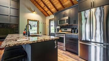 A kitchen with a large island, stainless steel appliances, and a wooden ceiling.