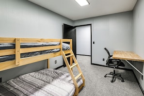 Ein Etagenbett mit einer Leiter, ein Schreibtisch mit Stuhl und eine Tür in einem Zimmer mit grauen Wänden und Teppichboden.