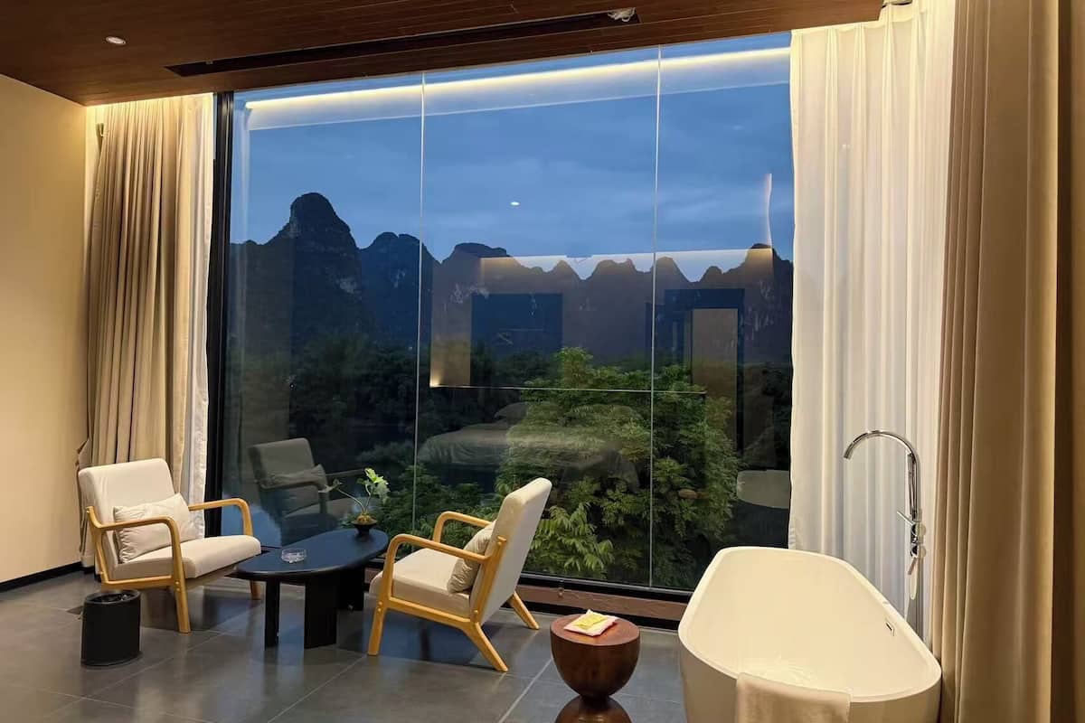 Una habitación moderna con un ventanal grande, dos sillas, una mesita y una bañera.