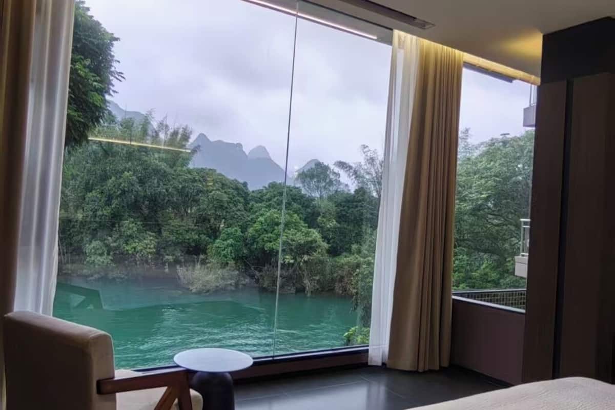 Un dormitorio con un ventanal grande, una cama, una silla y vistas a un paisaje natural.