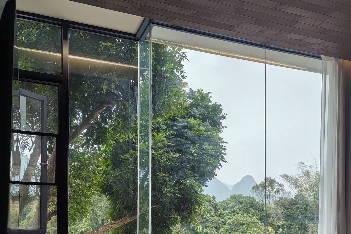 Un dormitorio con un ventanal grande, una cama y vistas a un río y un bosque.
